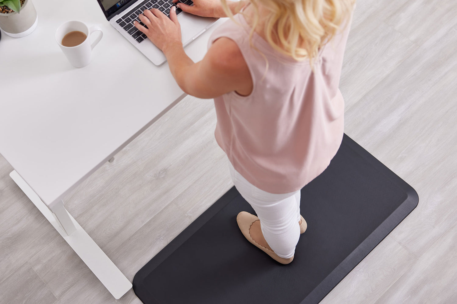 A woman standing on a Gorilla Grip anti-fatigue mat while working at her standing desk.