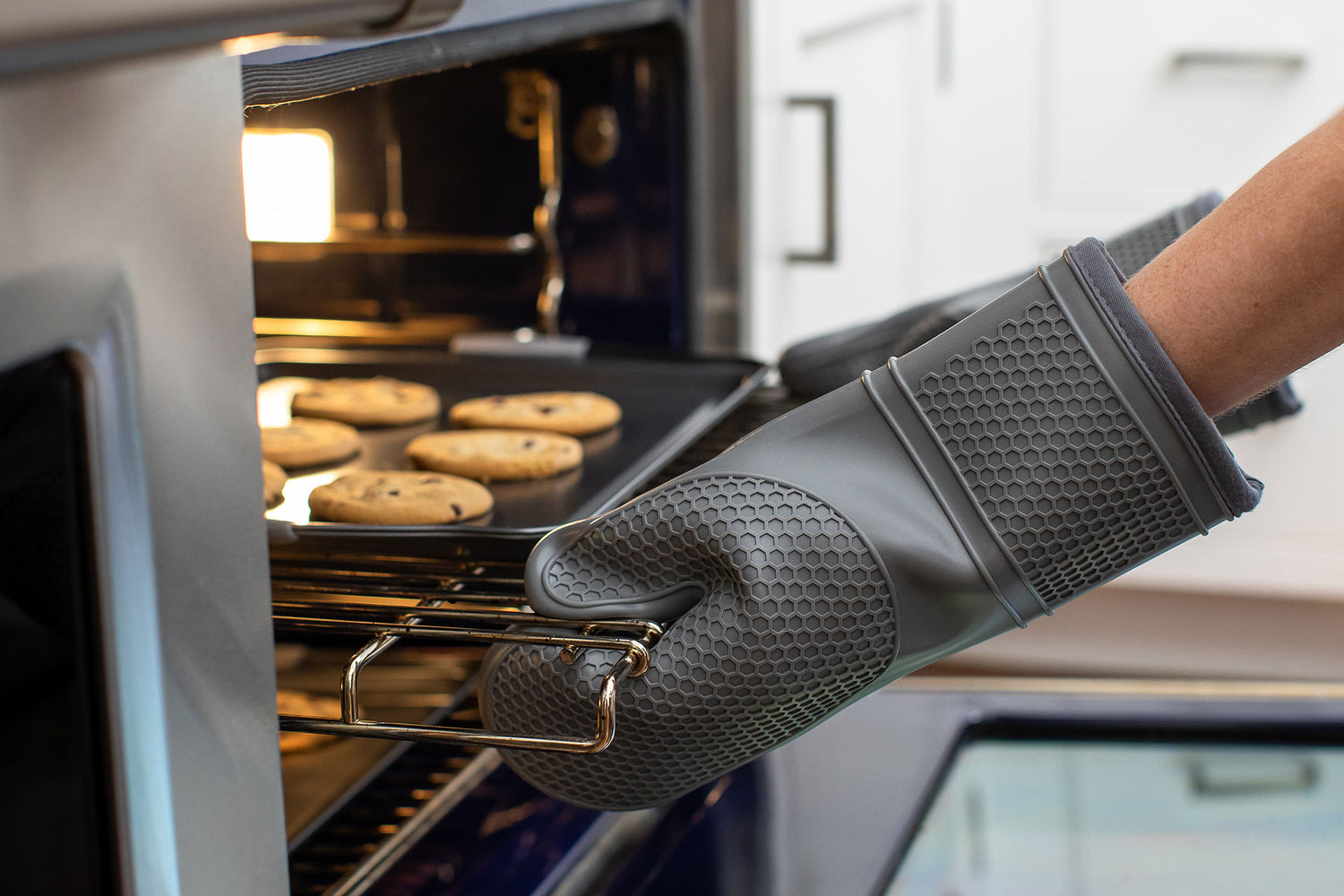 A person taking a rack of freshly baked cookies out of the oven using Gorilla Grip oven mitts.