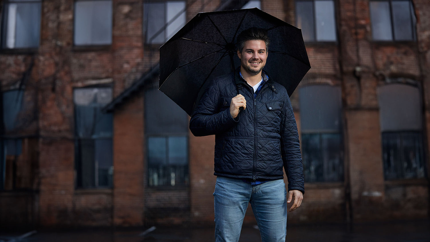 Man smiles holding a Gorilla Grip travel umbrella in a city setting
