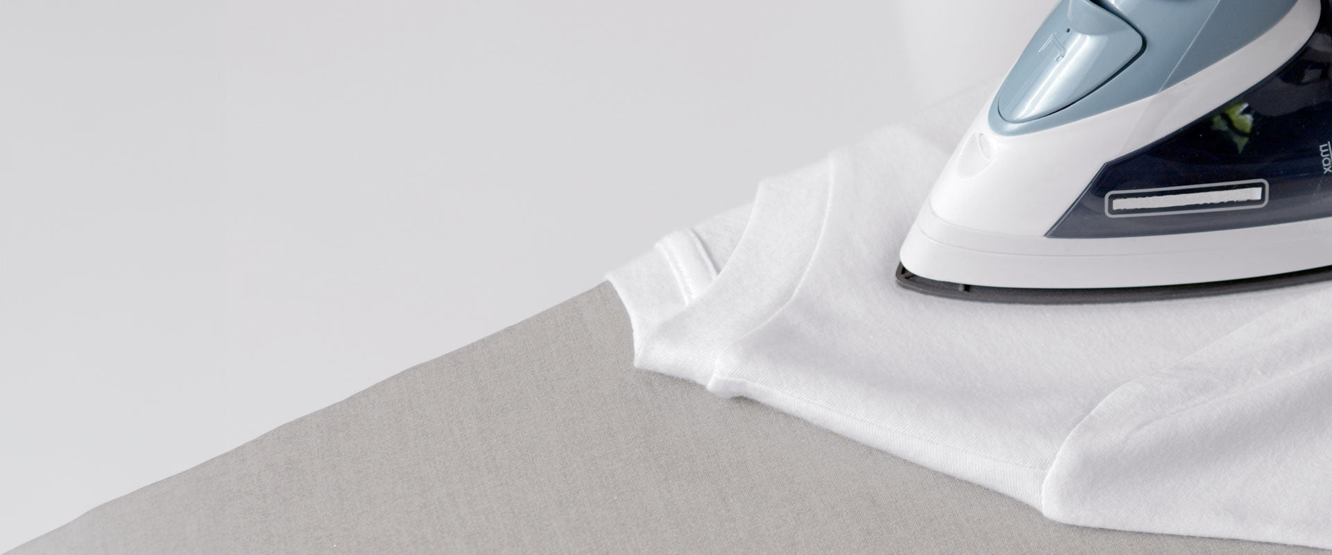 A modern iron on a white T-shirt, atop a gray ironing board with a Gorilla Grip ironing board cover