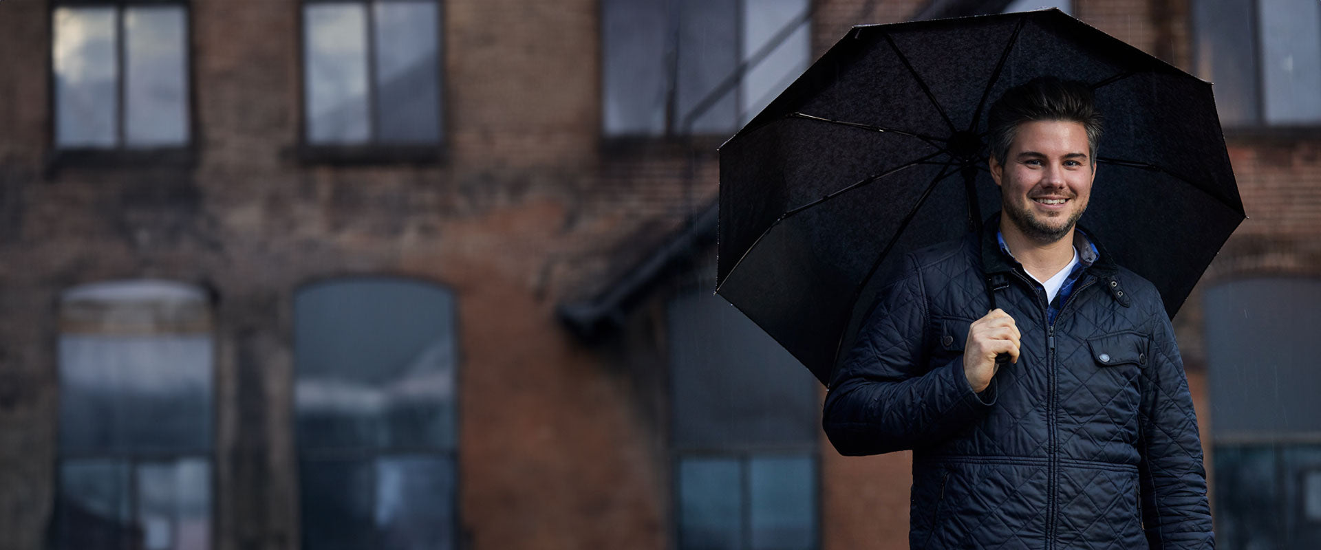 Man smiles holding a Gorilla Grip travel umbrella in a city setting